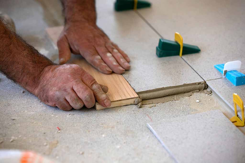 Main de carreleur qui pose du carrelage à l'aide d'une cale. Des taquets sont également utilisés pour aider le carreleur a faire des joints de précision.